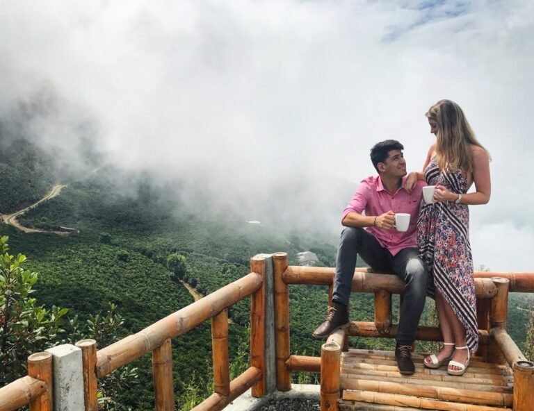 A couple standing together at a viewpoint deck amid misty green hills
