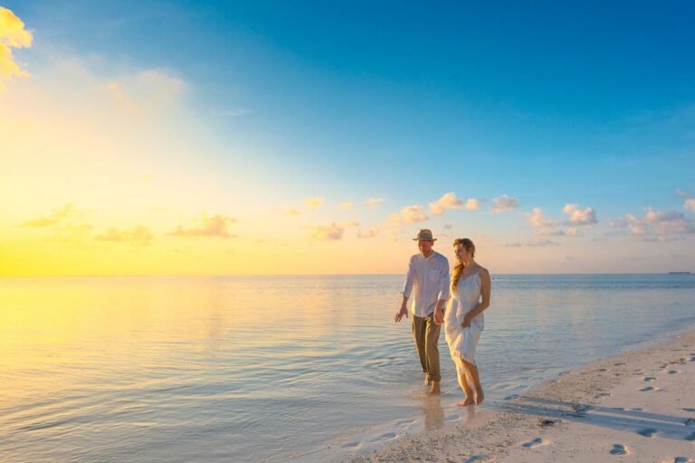 A couple walking hand in hand along a sandy beach at sunset
