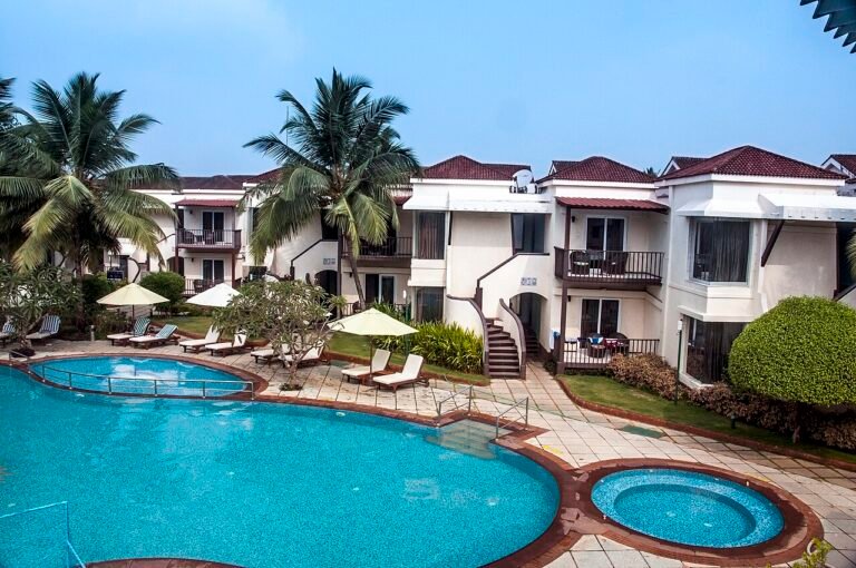 A resort swimming pool surrounded by palm trees and villa buildings