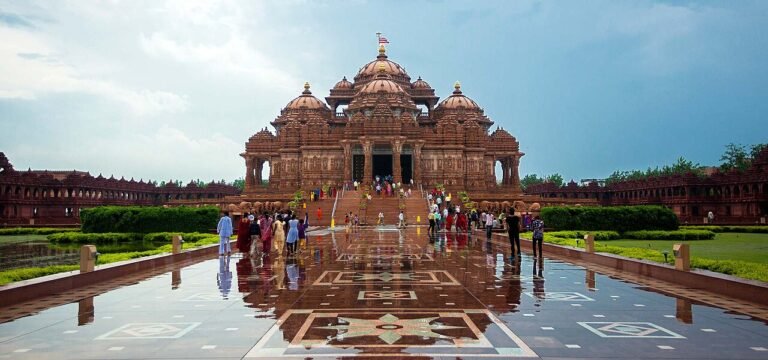 A white, intricately carved temple fronted by a broad plaza