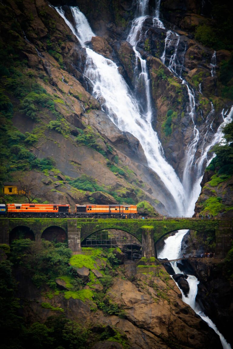 A train crossing a bridge beside a tall, multi-stream waterfall